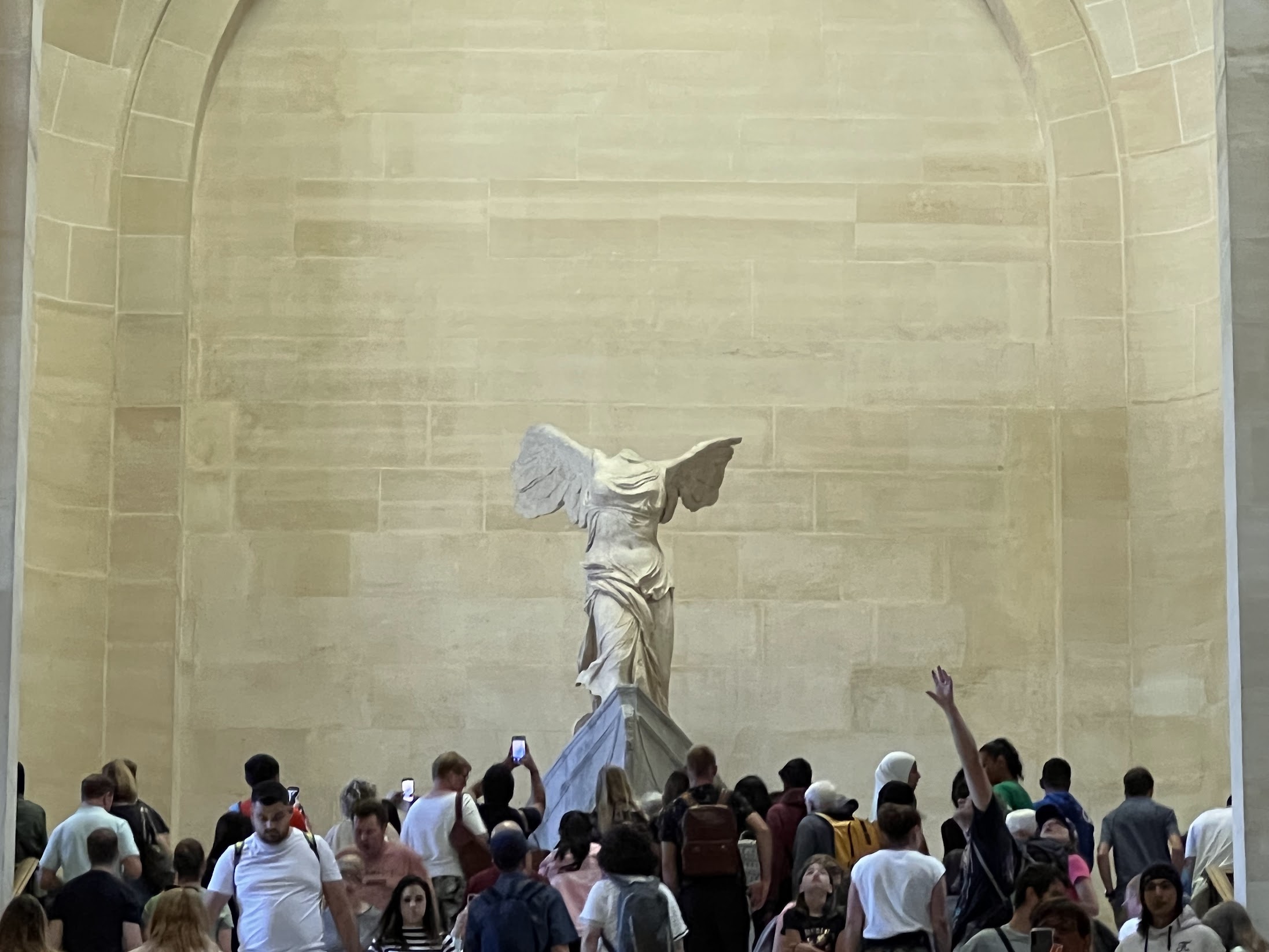 A photo of the venus statue in versailles but zoomed back to show all of the people in front of it. 